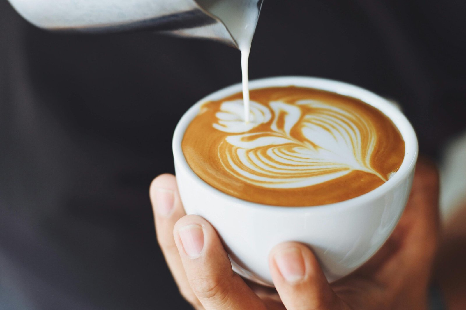 Close-up of a barista pouring milk to create latte art in a coffee cup.